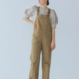 Camel-colored chino stretch overalls modeled on person, featuring large front patch pocket and adjustable shoulder straps for customizable fit