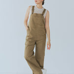 Camel-colored chino stretch overalls modeled on person, featuring large front patch pocket and adjustable shoulder straps for customizable fit