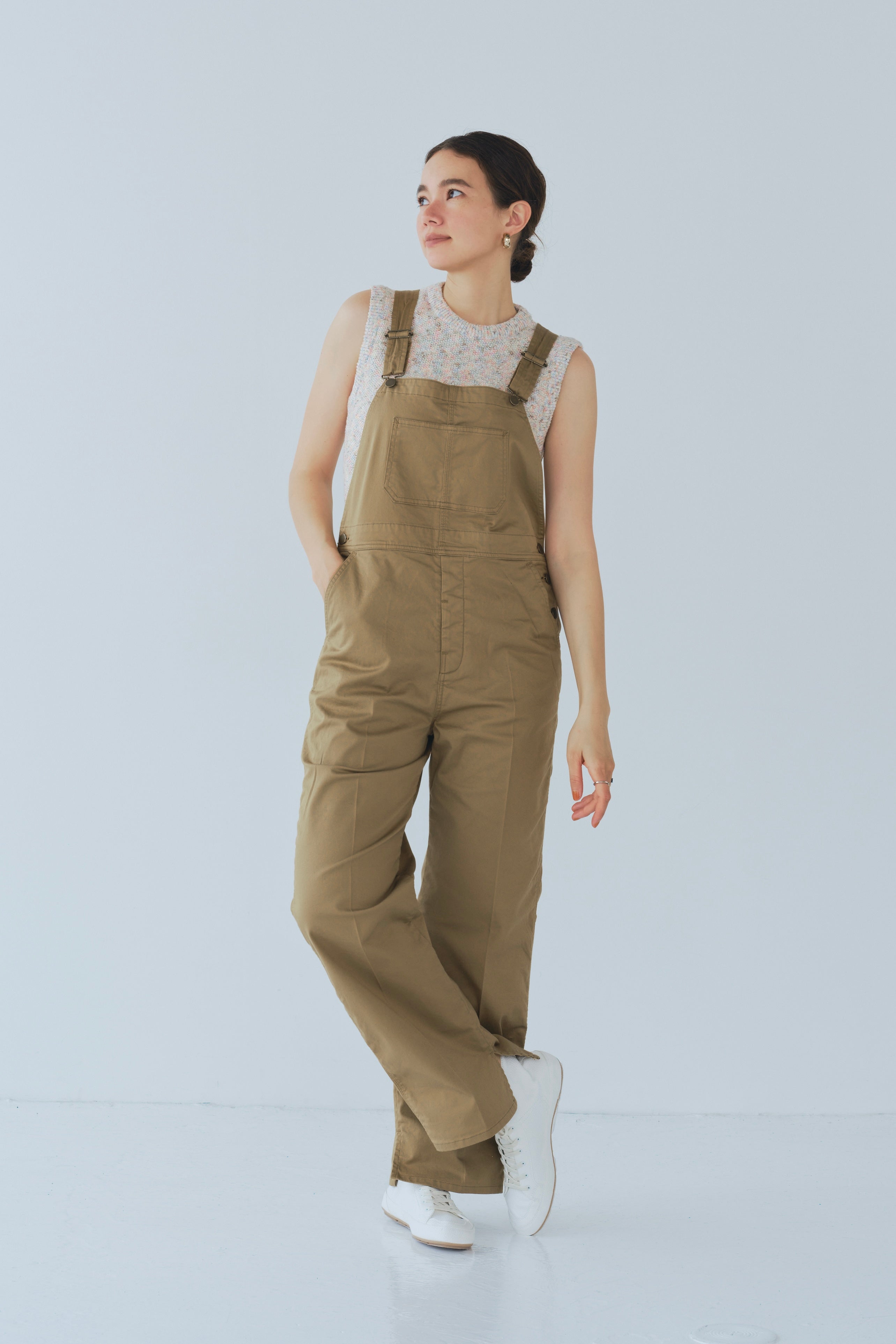 Camel-colored chino stretch overalls modeled on person, featuring large front patch pocket and adjustable shoulder straps for customizable fit